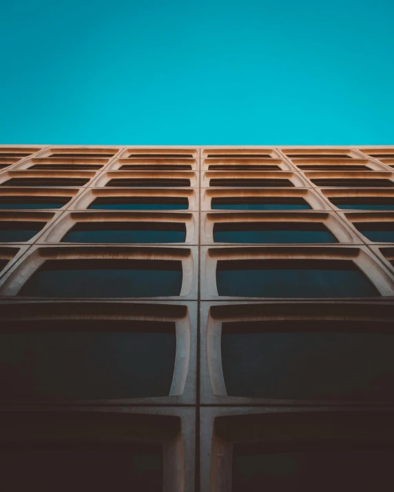 a tall building with a blue sky in the background, an album cover, unsplash contest winner, brown holes, rows of windows lit internally, brown and cyan color scheme, trending photo