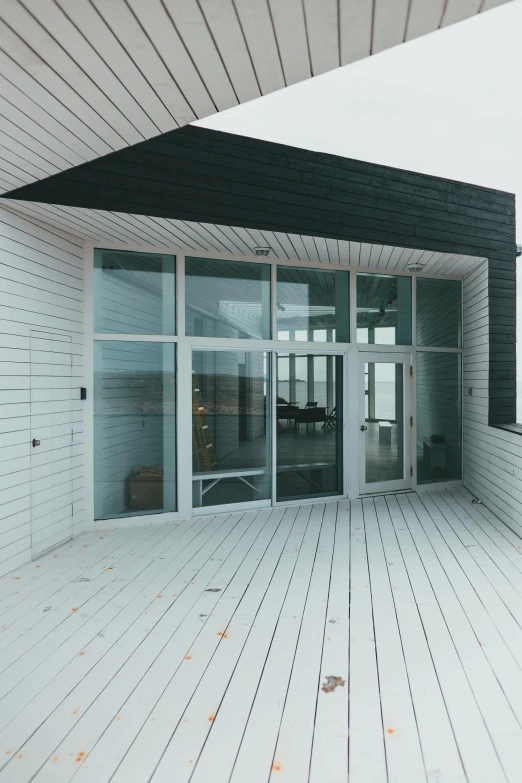 a white wooden deck with sliding glass doors, by Jaakko Mattila, unsplash, buildings covered in black tar, entrance, low quality photo, modeled
