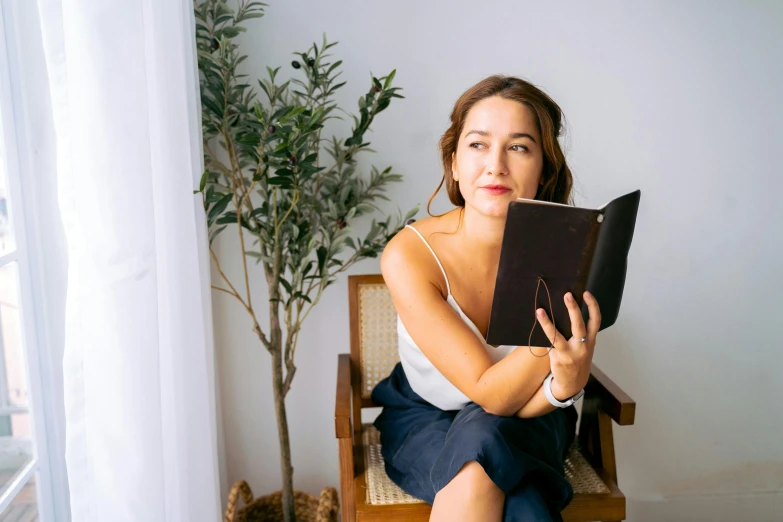 a woman sitting in a chair reading a book, a portrait, pexels contest winner, figuration libre, portrait image, holding notebook, product introduction photo, full faced