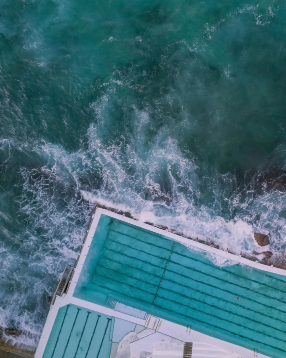 an aerial view of a swimming pool next to the ocean, inspired by Elsa Bleda, pexels contest winner, happening, violent stormy waters, bondi beach in the background, seafoam green, gif