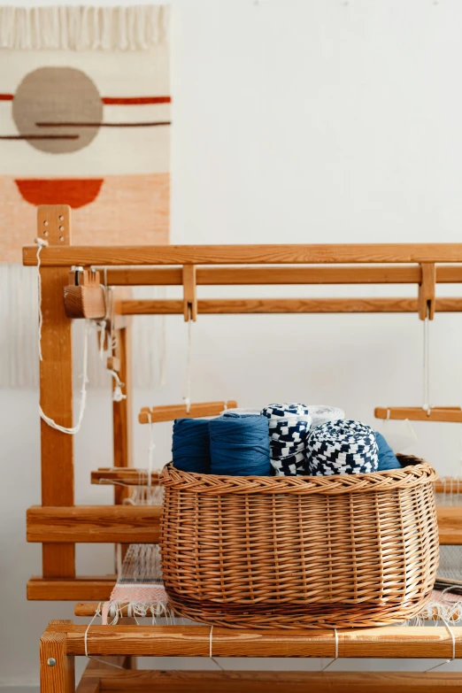 a basket sitting on top of a table next to a weaving machine, by Jessie Algie, trending on unsplash, arts and crafts movement, architectural digest, amber and blue color scheme, clean minimalist design, wooden supports