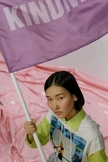 a woman holding a purple flag in front of a pink tarp, an album cover, inspired by Fei Danxu, trending on pexels, toiletpaper magazine, off - white collection, modelling, green flag