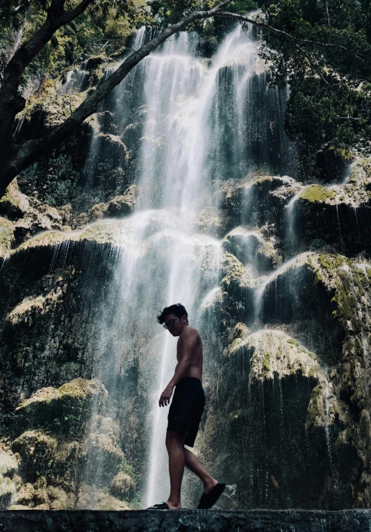 a man standing in front of a waterfall, an album cover, by Robbie Trevino, sumatraism, :: madison beer, maui, sad man, photo taken in 2018