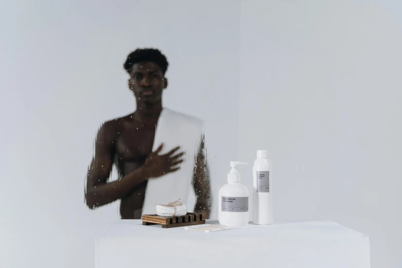 a man that is standing in front of a mirror, on a white table, dark grey skin, milk - bath effect, holding a bottle