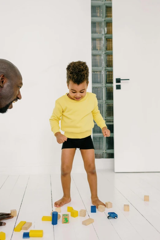 a man and a child playing with wooden blocks, by Nina Hamnett, pexels contest winner, minimalism, black and yellow tracksuit, wears shorts, light skinned african young girl, leaving a room