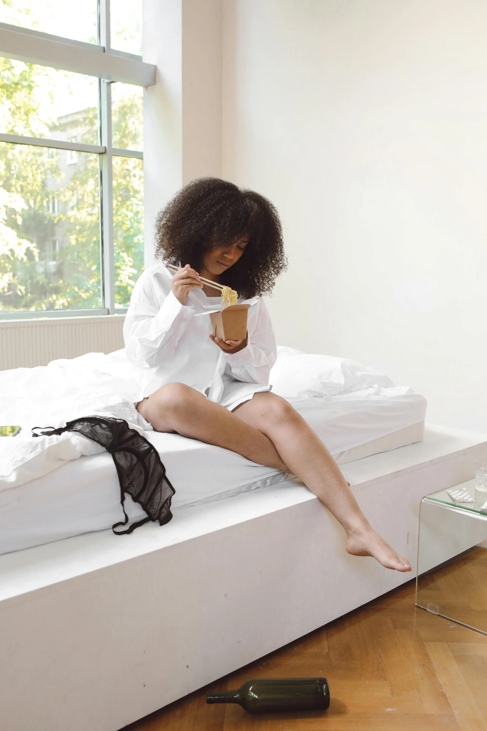 a woman sitting on top of a bed next to a window, eating, wearing nanotech honeycomb robe, ashteroth, performing