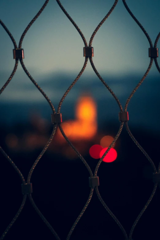 a close up of a chain link fence, a picture, by Adam Marczyński, pexels contest winner, glowing temple in the distance, blurry image, in jail, distant town lights