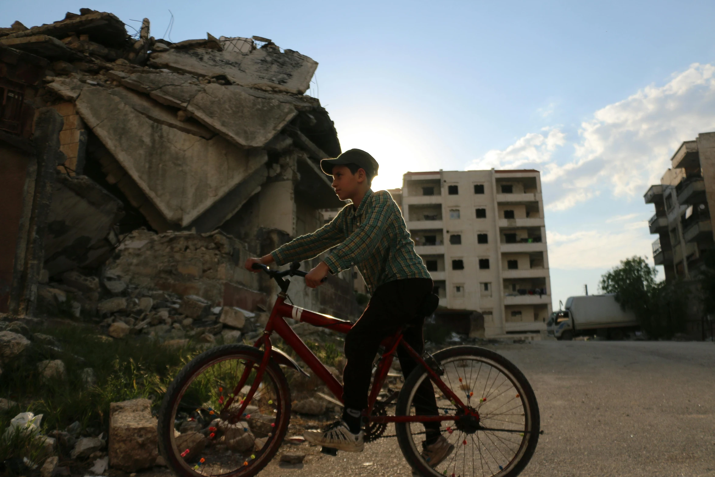 a boy riding a bike in front of a building, standing atop a pile of rubble, eytan zana, profile pic, ap