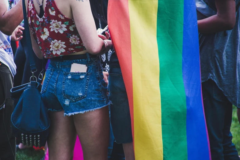 a group of people standing around a rainbow flag, trending on unsplash, wearing denim short shorts, woman holding another woman, background image, 🚿🗝📝