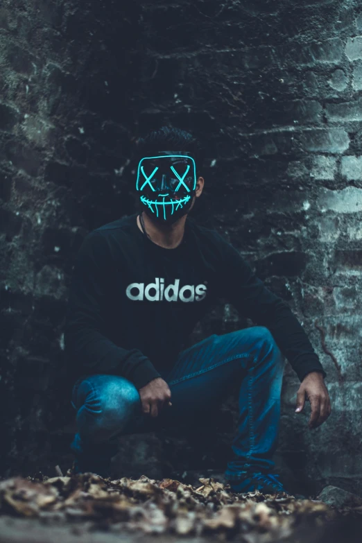 a man wearing a mask sitting on the ground, inspired by Alfred Freddy Krupa, pexels contest winner, graffiti, new adidas logo design, glow in the dark, plain background, modded