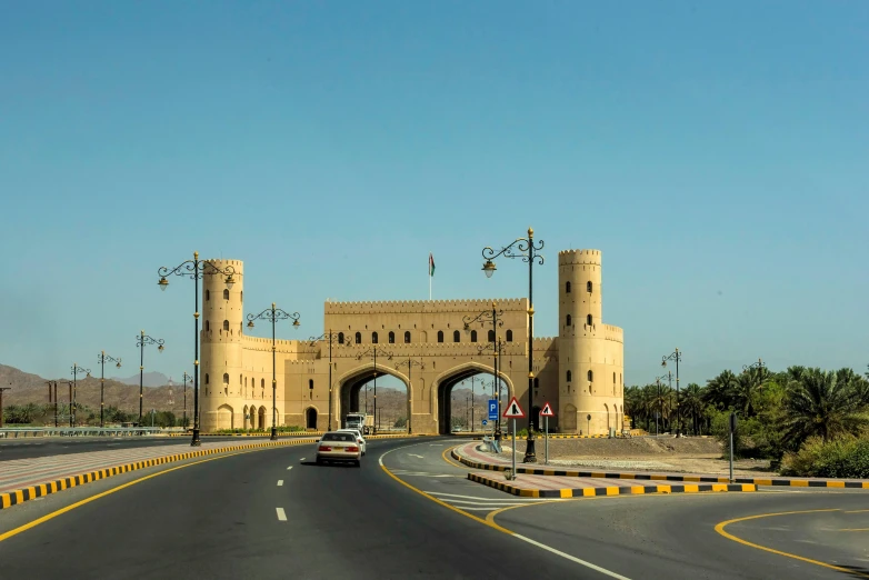 a car driving down a road next to a tall building, dau-al-set, aqueduct and arches, fortresses, tourist photo, exterior photo