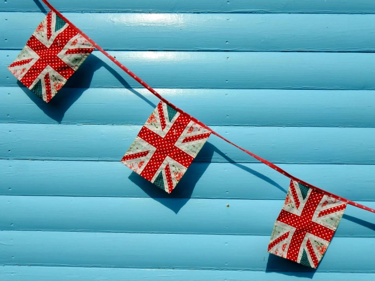 three flags hanging from a string on a blue wall, by Sylvia Wishart, unsplash, boris johnson gigachad, fully decorated, shack close up, squares