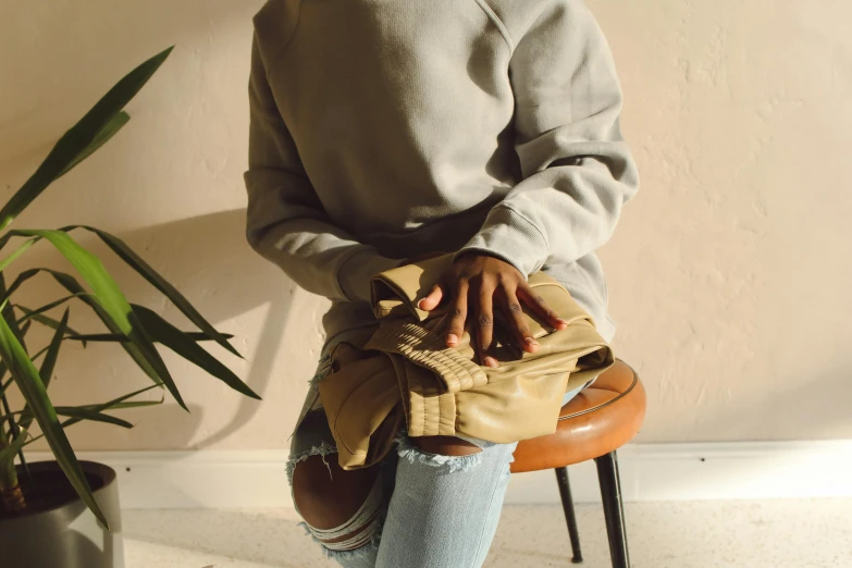 a woman sitting on a stool next to a potted plant, inspired by Sarah Lucas, trending on pexels, beige hoodie, holding arms on holsters, high angle close up shot, leather pouch