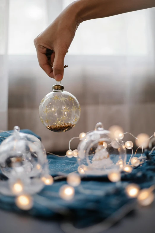 a person holding a glass ornament on top of a bed, light scatter, grey, fully decorated, medium - shot