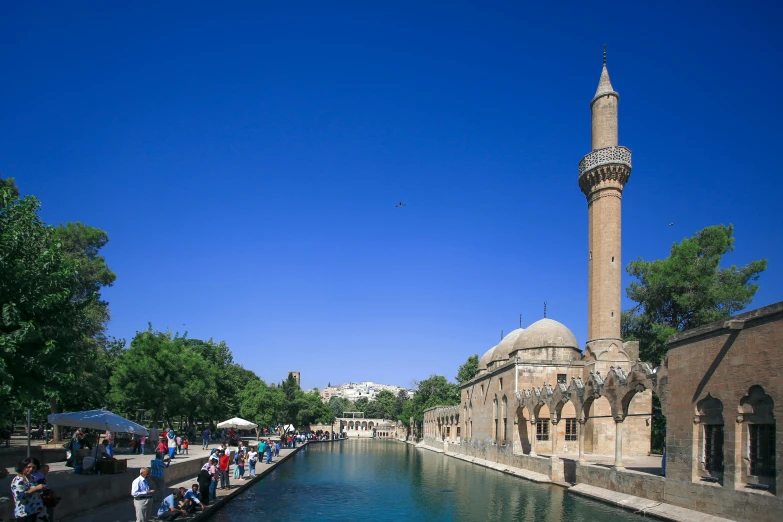 a group of people standing next to a body of water, by Abdullah Gërguri, pexels contest winner, hurufiyya, mardin old town castle, canal, blue sky, foster and partners