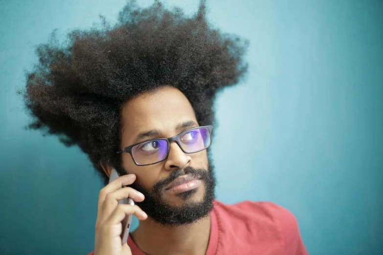 a man with a beard and glasses talking on a cell phone, by Washington Allston, pexels, fantastic realism, long afro hair, pompadour, thinking pose, an ancient