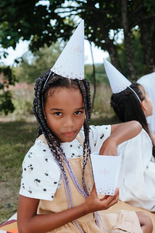 a group of young girls sitting on top of a blanket, by Alice Mason, unsplash, party hats, long black braids, wearing white chef hat, with brown skin