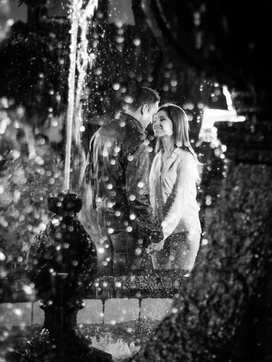 a black and white photo of a couple kissing in the rain, by Julia Pishtar, fountain, light snowfall, standing in a grotto, bokeh. i