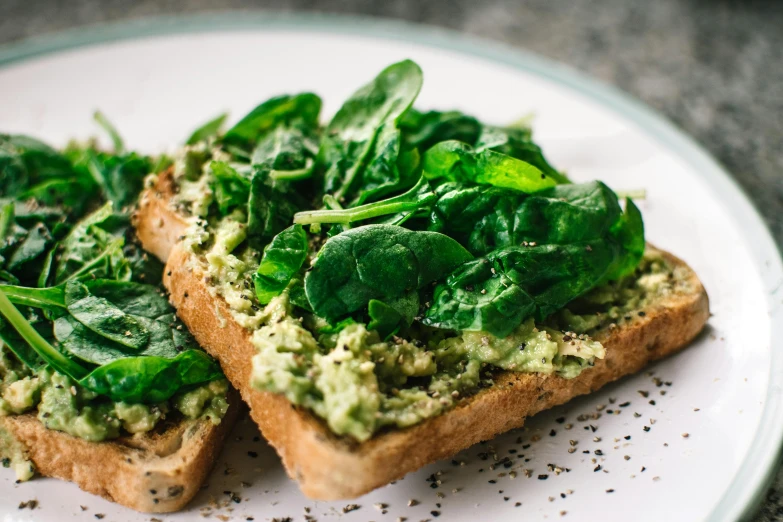 a white plate topped with two pieces of bread covered in spinach, by Tom Wänerstrand, trending on unsplash, emma watson as an avocado, bright castleton green, detail shot, battle toast