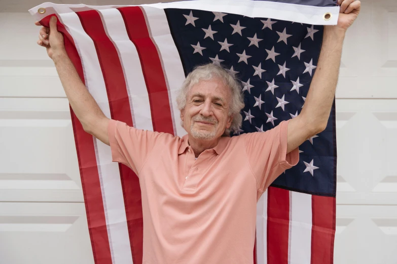 a man holding an american flag in front of a garage door, a photo, shutterstock, gray haired, celebration, danny de vito, portrait image