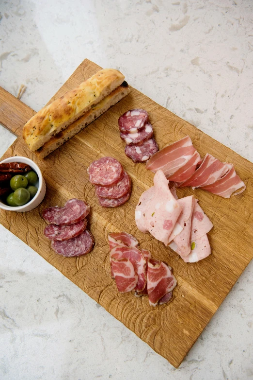 a wooden cutting board topped with meat and olives, inspired by Antonio Saura, medium angle, snacks, from left, casually dressed