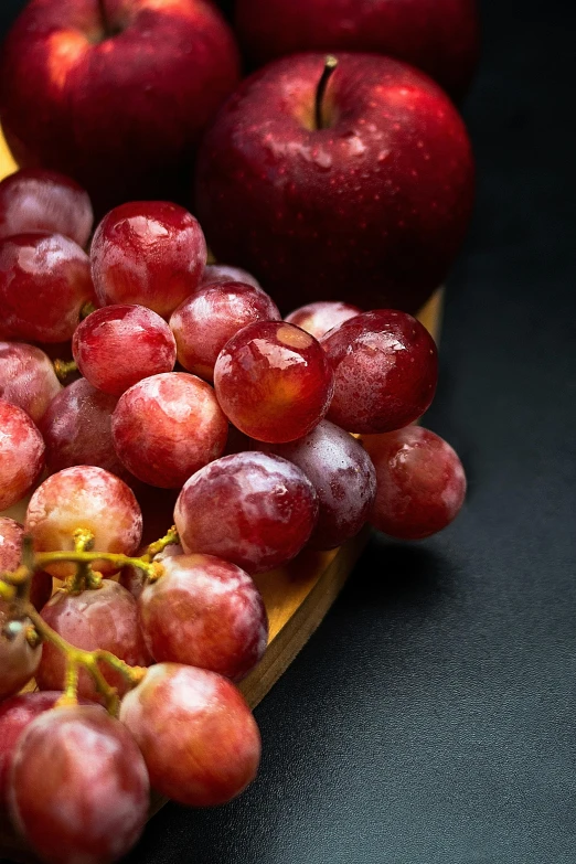 a bunch of grapes sitting on top of a wooden cutting board, with a black background, crimson themed, zoomed in