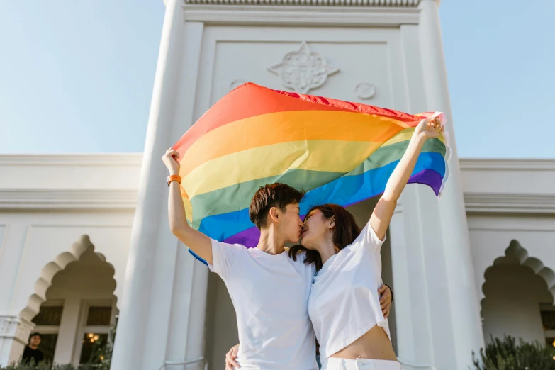 a man and woman holding a rainbow flag in front of a building, trending on pexels, cute boys, holding a white flag, couple on bed, 🚿🗝📝