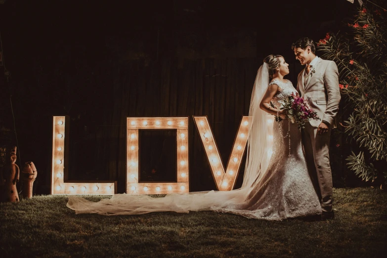 a bride and groom standing in front of a love sign, pexels contest winner, lit from the side, thumbnail, high quality image, ad image