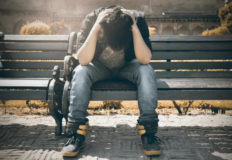 a man sitting on a bench with his head in his hands, pexels, wearing ragged clothing, teenager, derealisation, lgbtq