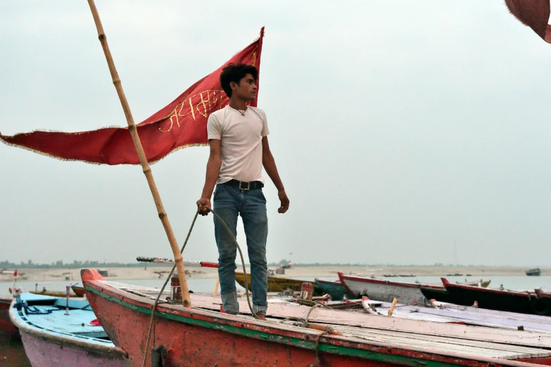 a man standing on top of a boat holding a red flag, by Kailash Chandra Meher, flickr, gutai group, slightly muscular, promo image, thumbnail, dressed in a worn