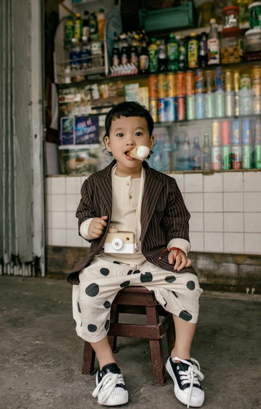 a little boy sitting on a stool eating an ice cream cone, inspired by Xie Huan, pexels contest winner, dressed with long fluent clothes, polka dot, in style of lam manh, market