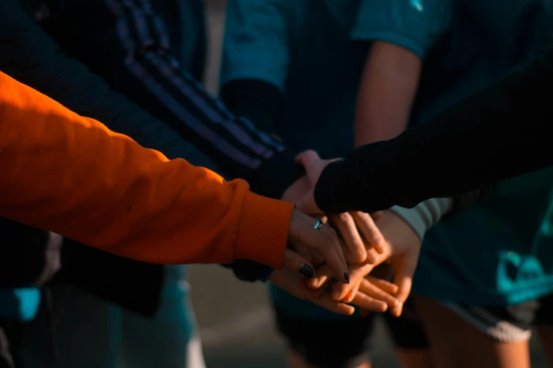 a group of people holding hands in a circle, by Jesper Knudsen, pexels, antipodeans, orange and teal, tournament, early in the morning, thumbnail