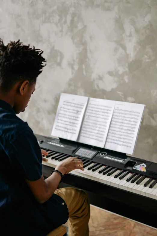 a young man sitting in front of a piano, trending on pexels, black teenage boy, sheet music, using synthesizer, paul barson