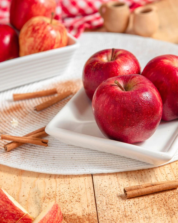 a white plate topped with red apples on top of a wooden table, inspired by Myles Birket Foster, shutterstock contest winner, cinnamon, product display photograph, square, ilustration