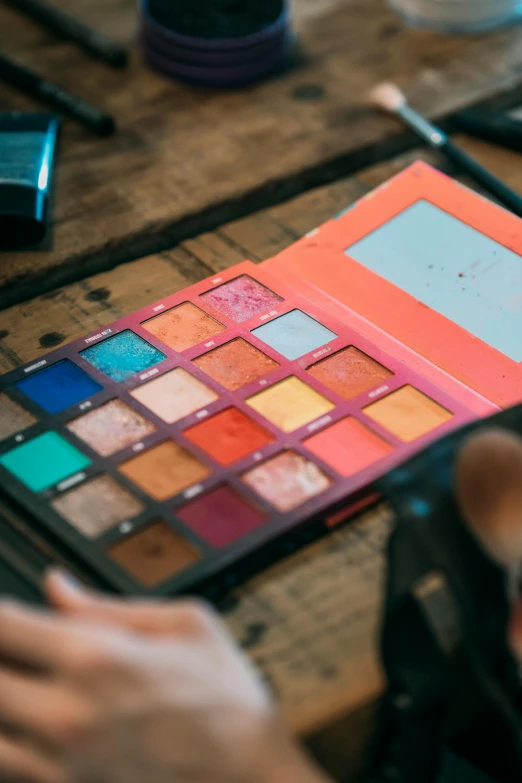 a person sitting at a table with a makeup palette, inspired by Elsa Bleda, trending on pexels, teal and orange, inspect in inventory image, eye shadow, grungy; colorful