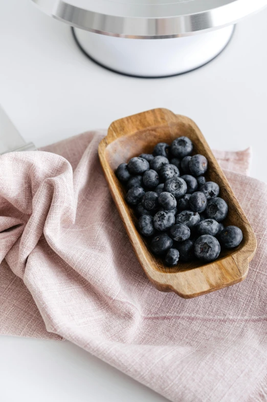 a wooden bowl filled with blueberries on top of a pink napkin, by Lucette Barker, trending on unsplash, grey, at the counter, snacks, focus on full - body