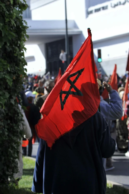 a group of people holding flags in front of a building, black on red, pentagrams, moroccan, over his shoulder
