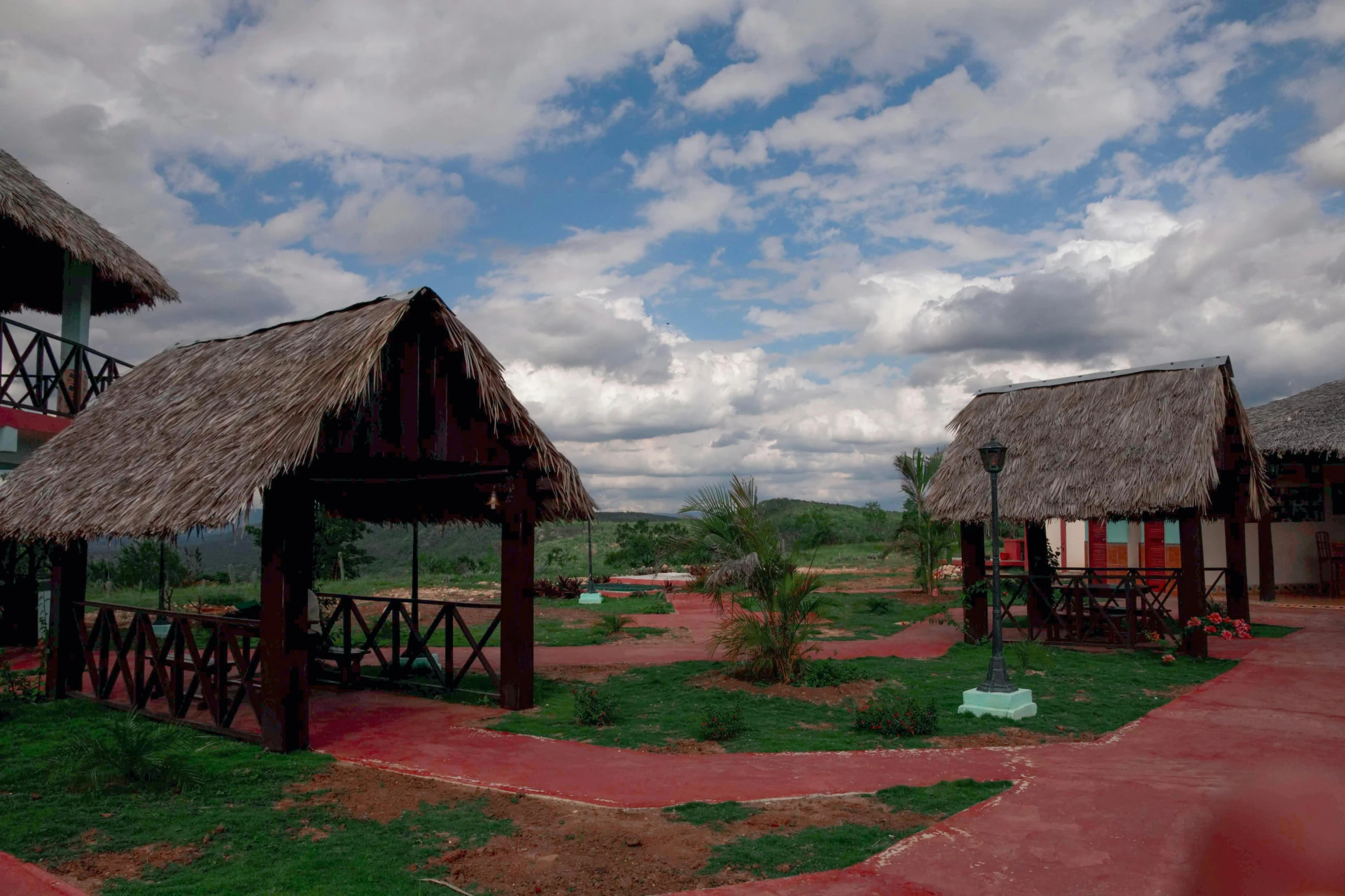 a couple of thatched huts sitting on top of a lush green field, cuban setting, adventure playground, image