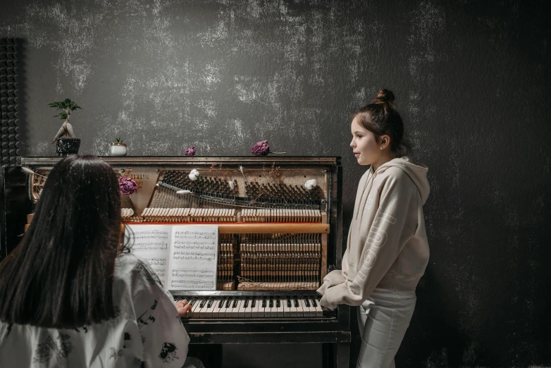 a woman standing in front of a piano, by Lucia Peka, pexels contest winner, girl in studio, annoying sister vibes, on a gray background, schools
