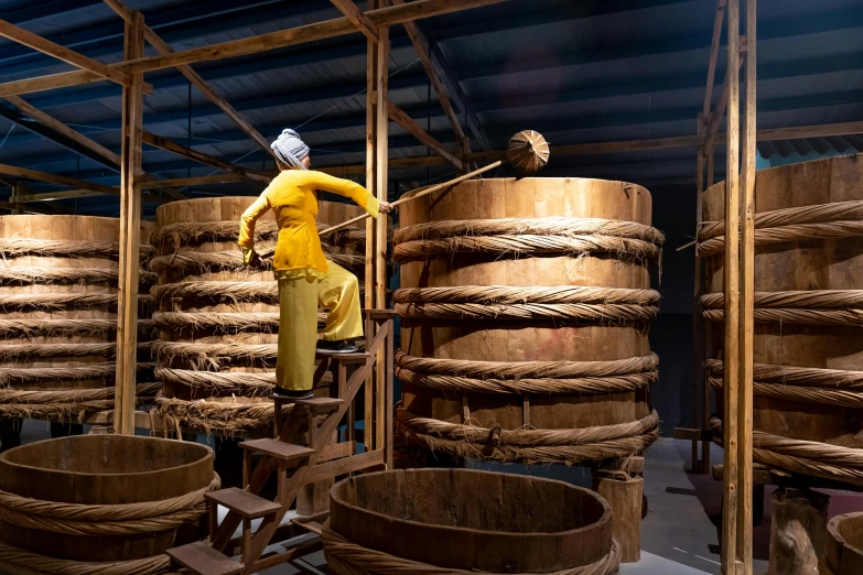 a man that is standing on a ladder, inspired by Li Di, wooden crates and barrels, with yellow cloths, single clay museum sculpture, 2 0 2 2 photo