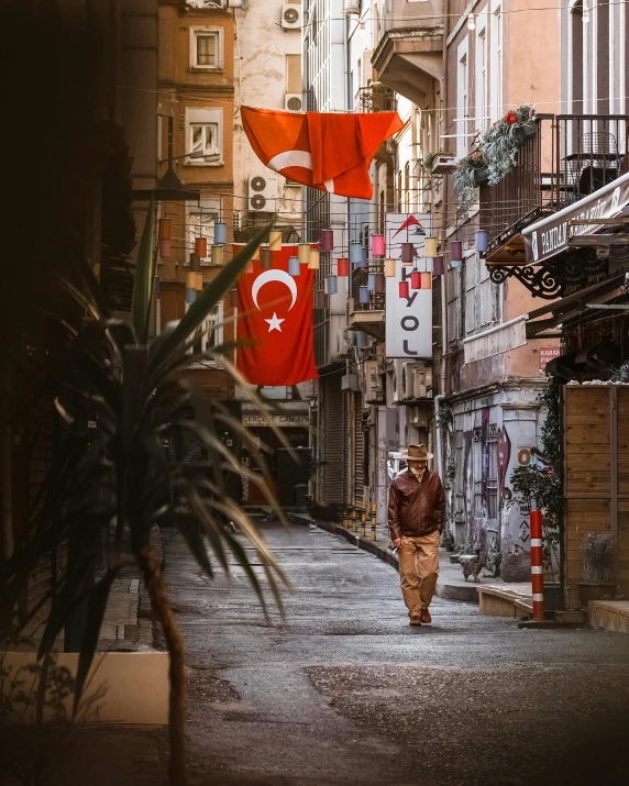 a man walking down a street next to tall buildings, a colorized photo, pexels contest winner, hurufiyya, red banners, turkey, 🚿🗝📝, in an alley
