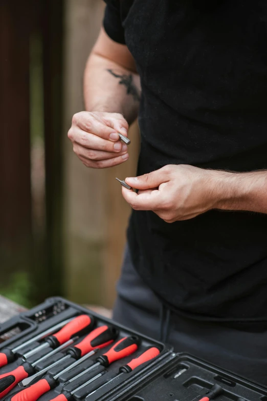 a man standing in front of a table filled with tools, smoking a joint, outdoors, serrated point, quick assembly