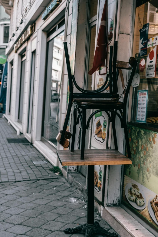 a chair sitting on top of a wooden table in front of a store, by Niko Henrichon, istanbul, two hang, small steps leading down, storefront