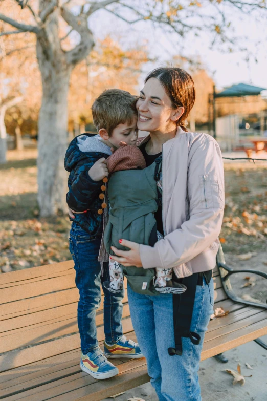 a woman holding a child on top of a wooden bench, holding arms on holsters, walking at the park, profile image, brand