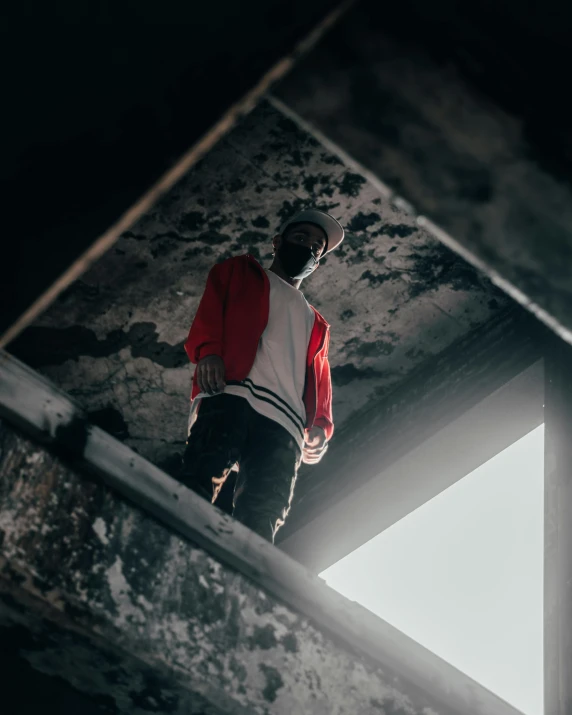 a man in a red jacket standing on a ledge, an album cover, unsplash contest winner, ceiling hides in the dark, techwear look and clothes, cement, concerned