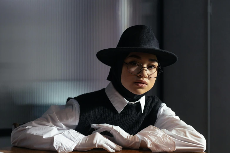 a person sitting at a table with a hat on, a character portrait, inspired by Bernardino Mei, unsplash, ashcan school, dressed as schoolgirl, muslim, museum photo, wearing gloves