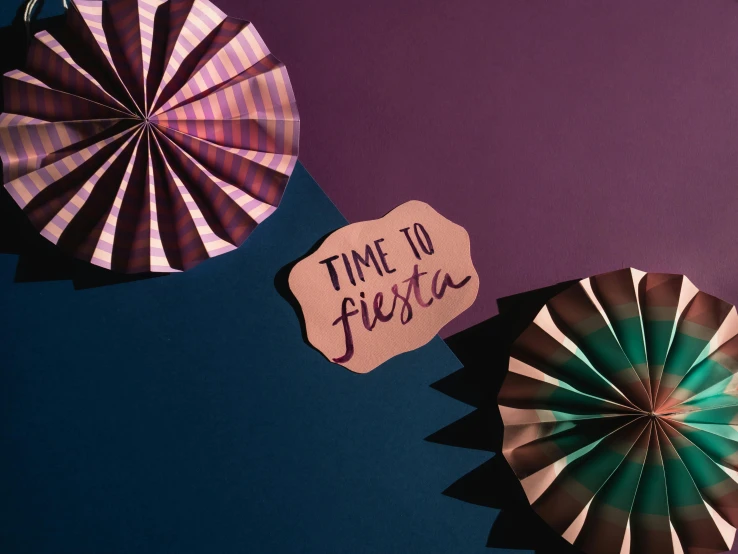 a couple of paper fans sitting on top of a table, by Julia Pishtar, graffiti, gradient black to purple, trendy typography, festive, copper and deep teal mood