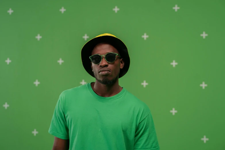 a man wearing a hat and sunglasses standing in front of a green wall, a picture, ( ( dark skin ) ), green theme, luts, a green