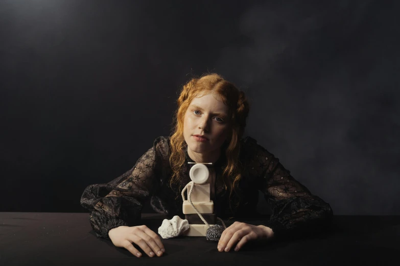 a woman with red hair sitting at a table, an album cover, inspired by Lasar Segall, statue of a cubes and rings, 2022 photograph, standing with a black background, hammershøi