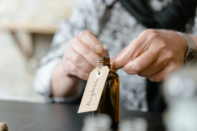 a close up of a person putting a tag on a bottle, unsplash, renaissance, local conspirologist, brown, oud, older woman